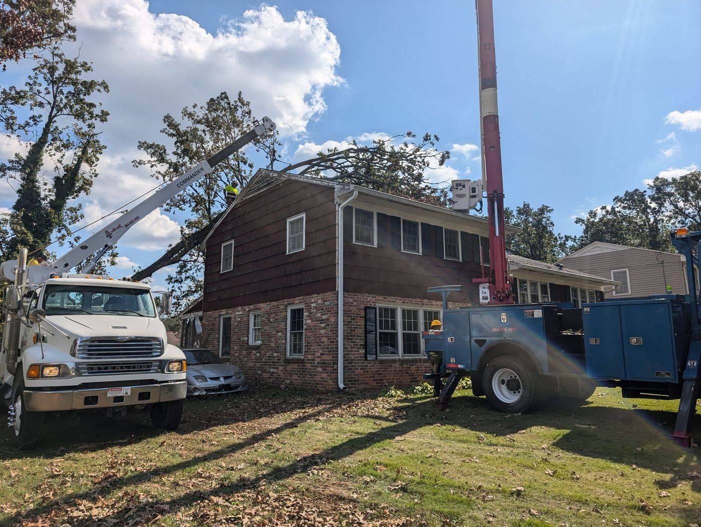 Embark crane and bucket trucks removing a storm-felled tree from a roof